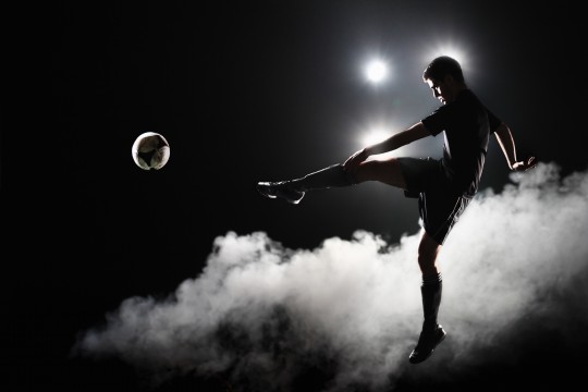 Soccer player kicking the ball at night on stadium
